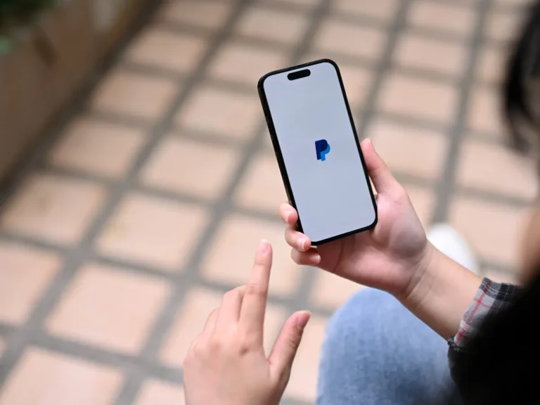 A person holding a mobile phone and paying with PayPal