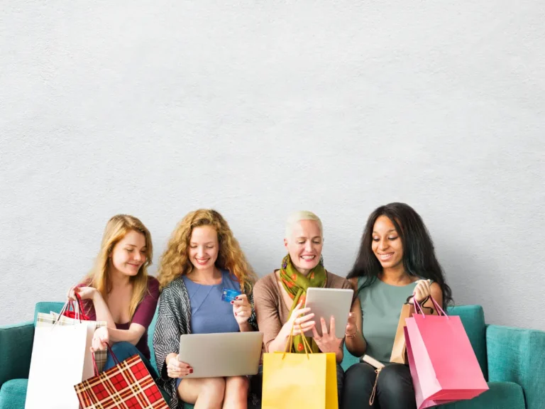 A group of women is sitting together with shopping bags, looking at online deals.