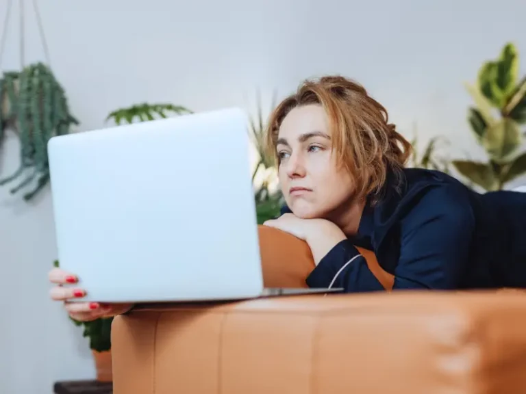 A sad woman looks at a laptop.