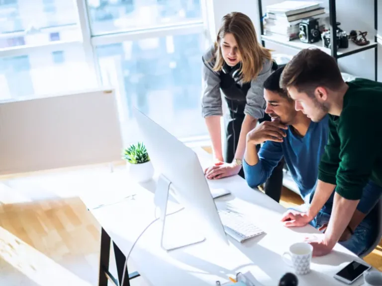 Three people looking at a computer at their workplace.