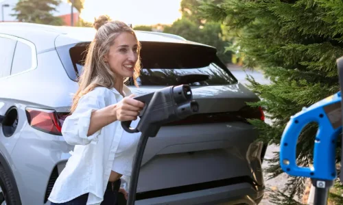 A woman plugs in an electric car plug into a charging station.