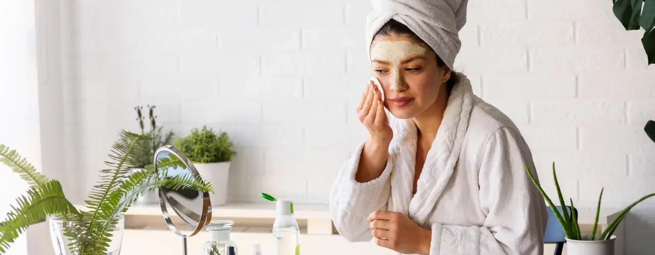 Success Story – Isispharma 1 A women sits in front of a mirror and applies different beauty cremes to her face.