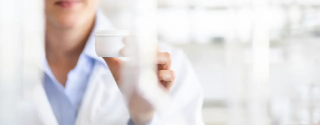Success Story – Isispharma 2 A scientist holding a pot of skin cream in a laboratory