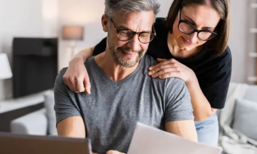 A woman and a man look at their tax papers in front of a computer